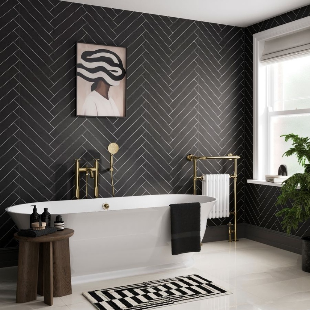 Lifestyle image of the Showerwall Laminate Black Velvet 2400mm x 600mm Herringbone Tile Effect Wall Panel - SWT14 installed across a large bathroom wall with freestanding bathtub, floorstanding bath shower mixer, and traditional radiator